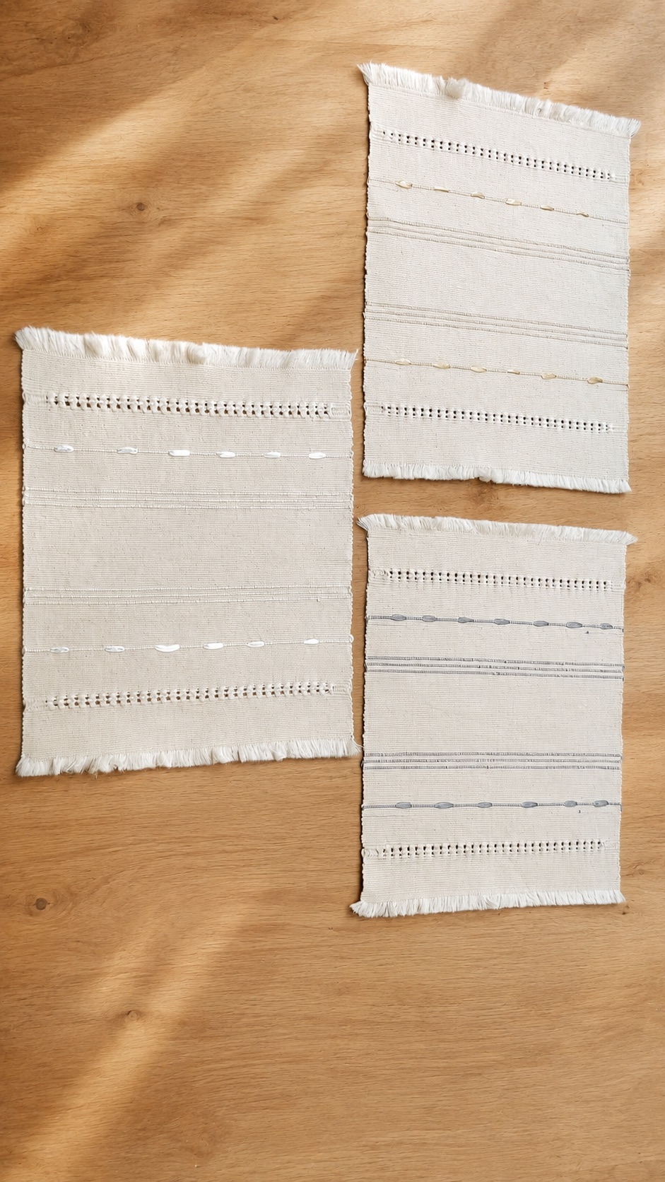 Tres individuales Cinta de Dilia Suárez en tonos marfil, gris y natural sobre mesa de madera